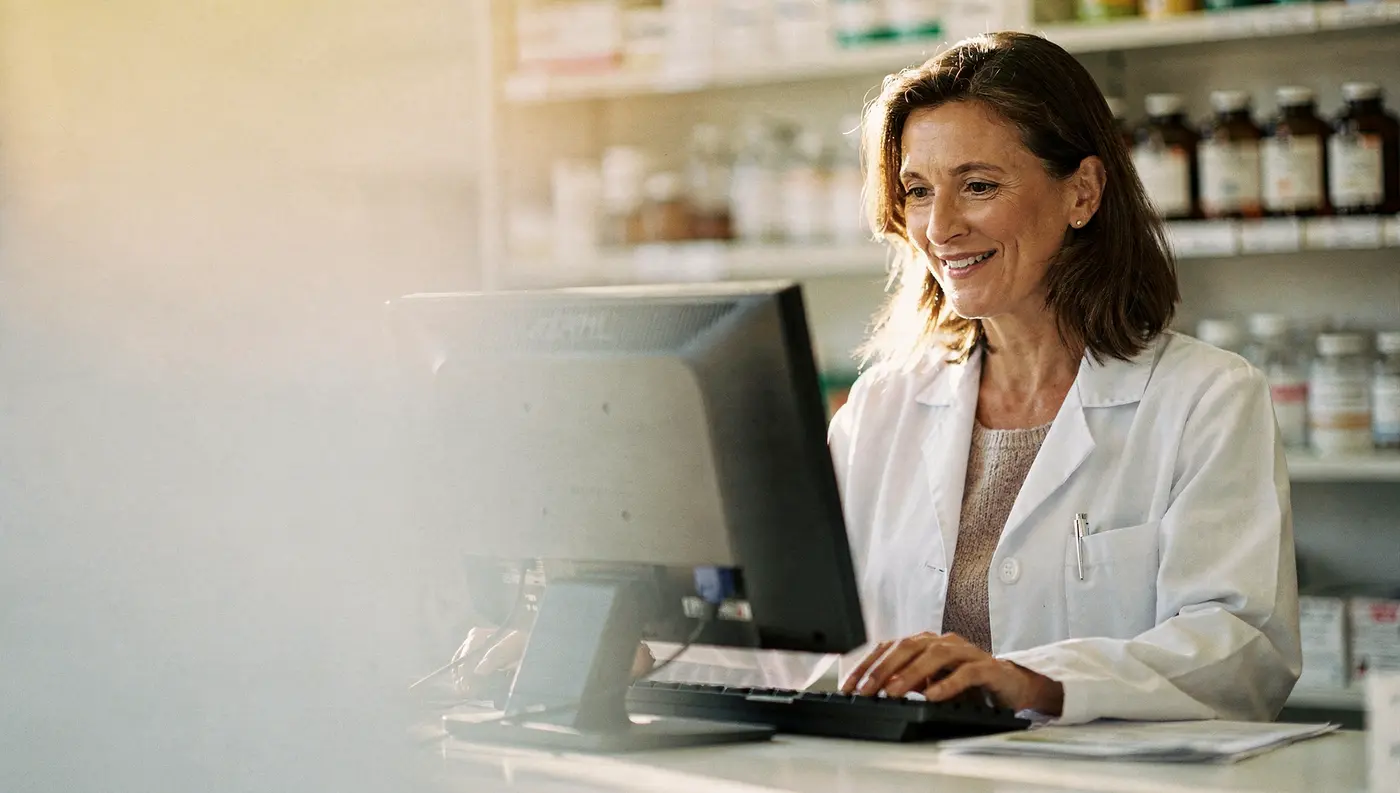 A clinician smiling at her computer at the front counter in soft morning light